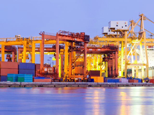 Panorama of Industrial Container Cargo freight ship with working crane bridge in shipyard at dusk for Logistic Import Export background